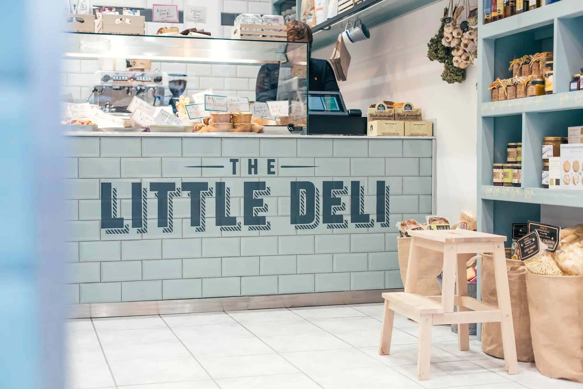 The Little Deli in hitchin, tiled county with fresh foods, and person serving.