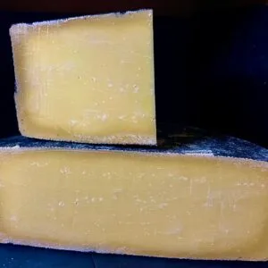 Two aged cheese wheels stacked on dark background