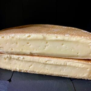 Halved wheel of soft cheese on black background