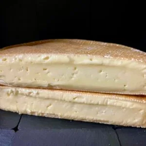 Halved wheel of soft cheese on black background