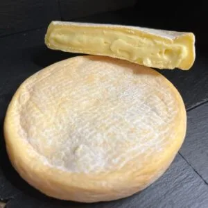 Whole and sliced soft cheese on dark background