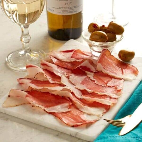 Sliced cured ham, olives, and wine on table
