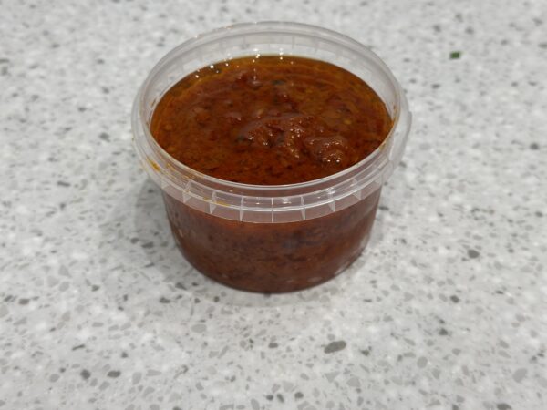 Plastic container filled with spicy red sauce on countertop