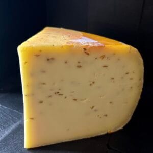 Cumin seeds infused cheese wedge on dark background