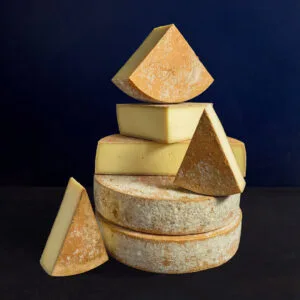 Stacked assorted cheese wheels on dark background