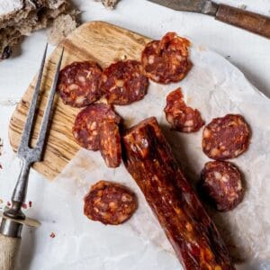 Sliced spicy chorizo on wooden board with bread crumbs