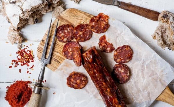 Sliced spicy chorizo on wooden board with bread crumbs