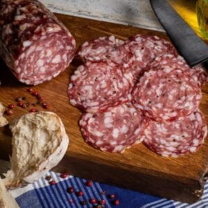 Sliced salami with bread on wooden board, rustic style