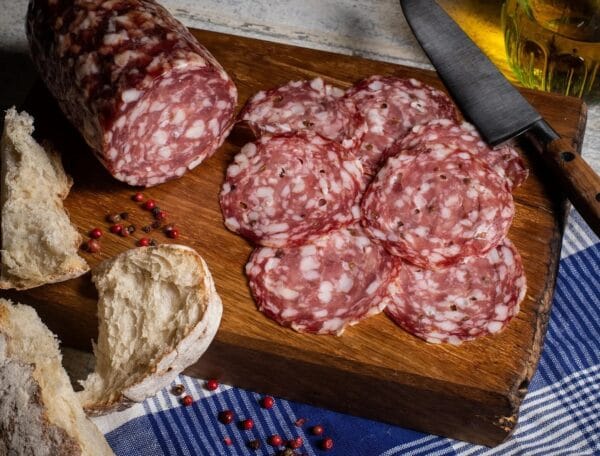 Sliced salami with bread on wooden board, rustic style