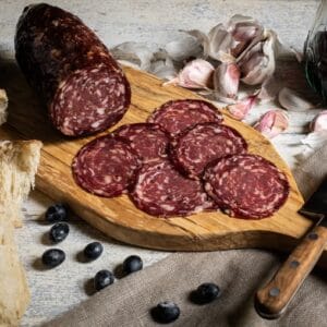 Sliced salami on wooden board with wine and garlic