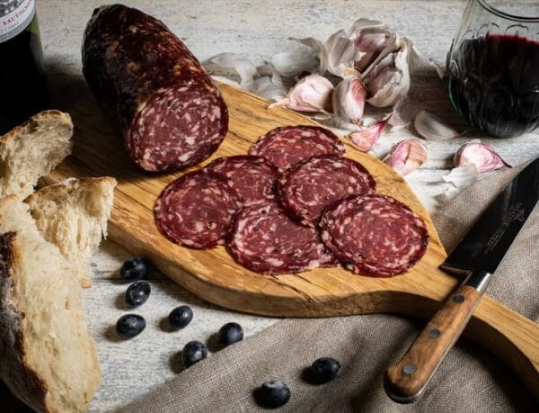 Sliced salami on wooden board with wine and garlic