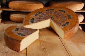 Whole and sliced aged cheese wheels on wooden table