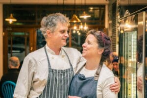 Two chefs smiling together in a warmly lit restaurant