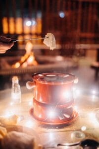 A hand dipping bread into a red cheese fondue pot